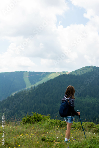 Young girl with backpack enjoying sunset on peak mountain. Girl happy tourist on top of a mountain enjoying valley view before sunset. excited little girl on a camping trip in green forest