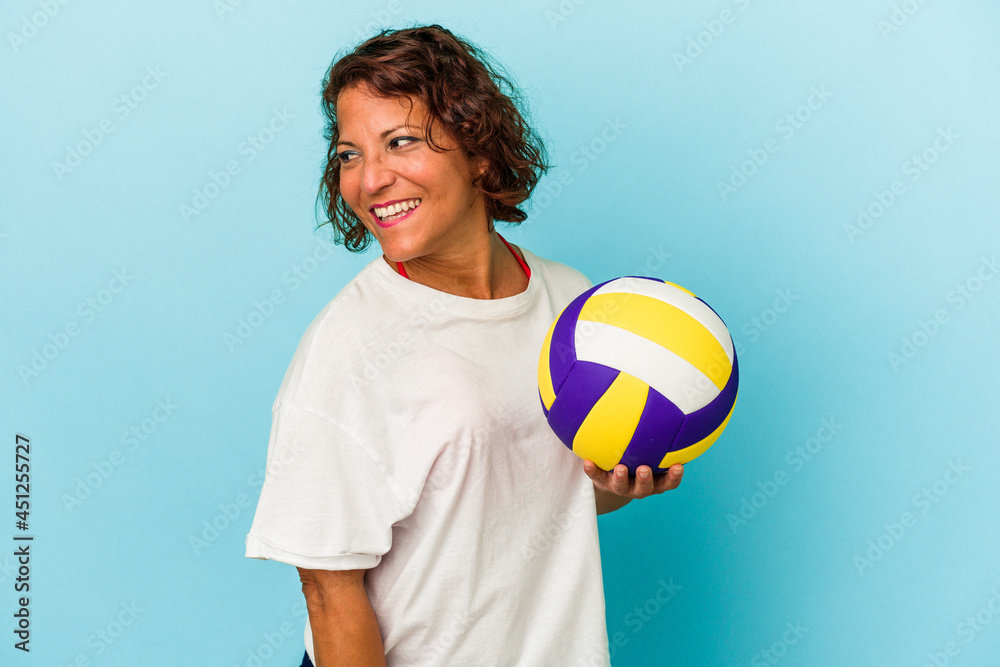 Middle age latin woman playing volleyball isolated on blue background looks aside smiling, cheerful and pleasant. Middle age latin woman playing volleyball isolated on blue background looks aside smiling, cheerful and pleasant.