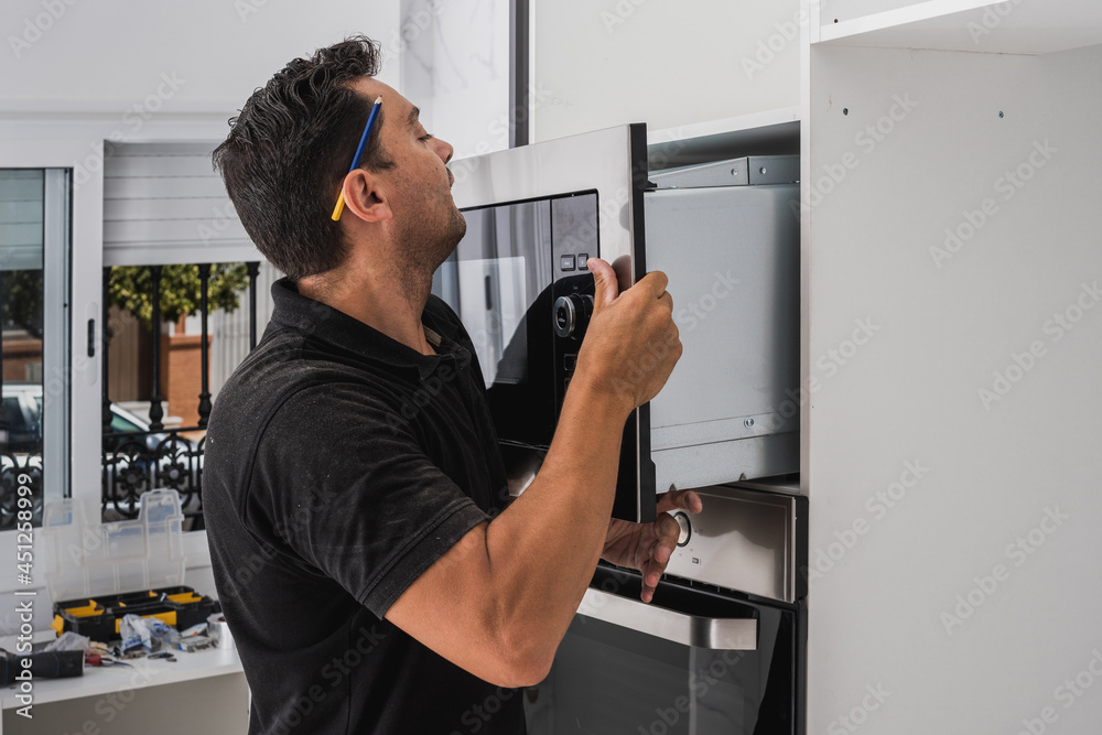 Man placing a microwave inside the hole of a new kitchen cabinet Man placing a microwave inside the hole of a new kitchen cabinet