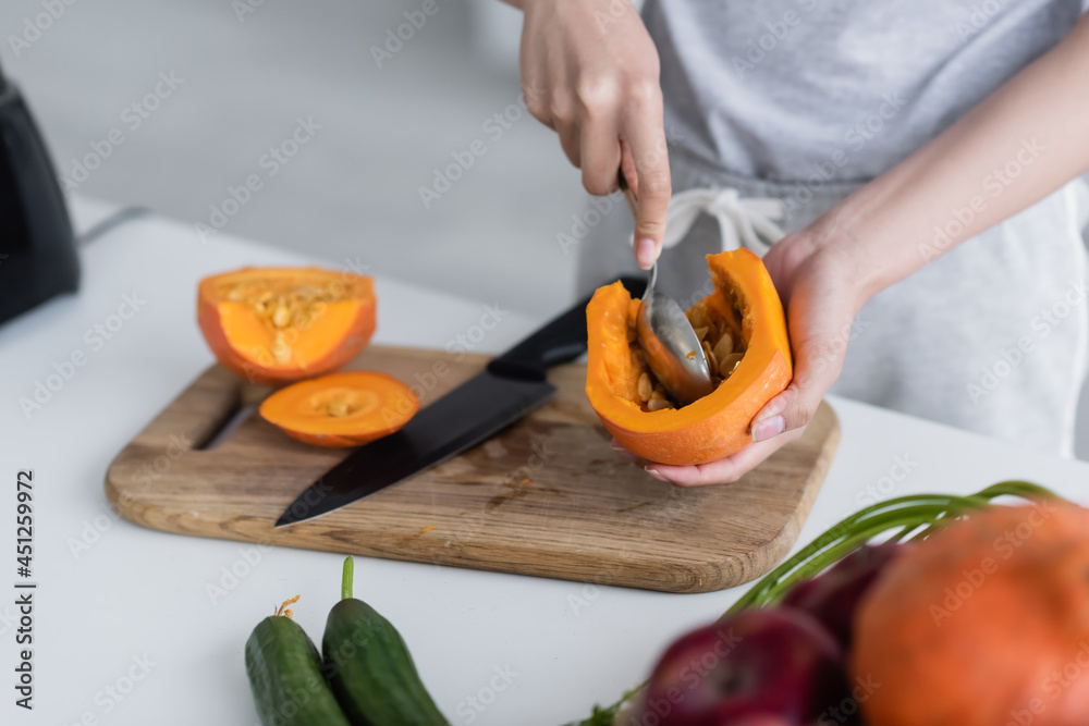 cropped view of woman cleaning out ripe pumpkin near fresh cucumbers and blurred apples. - obrazy, fototapety, plakaty 