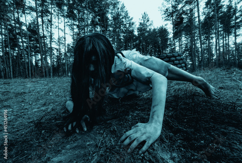 Girl in image of scary zombie crawls on ground in dark forest.