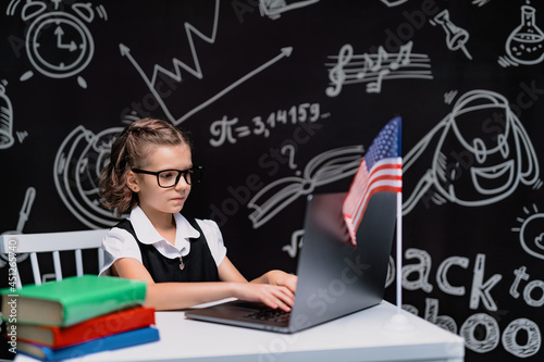beautiful little schoolgirl at desk against black background with USA flag