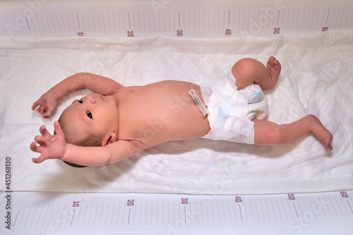 A newborn baby in diapers on a white changing table with a ruler with a Moro reflex photo