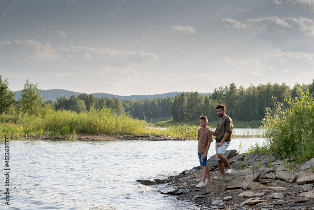 Father and son standing by lake while enjoying summer vacation in the country Father and son standing by lake while enjoying summer vacation in the country