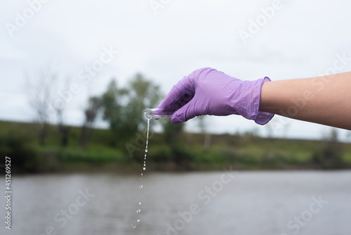 Water pollution concept. Woman a scientist takes a water sample from a river close up.