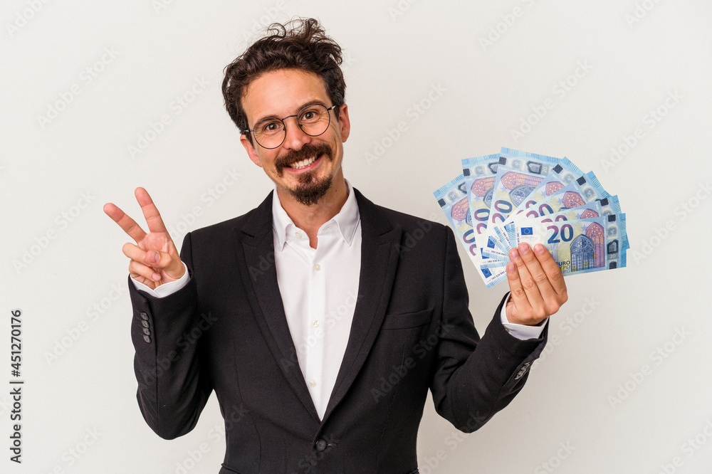 Young caucasian man holding banknotes isolated on white background joyful and carefree showing a peace symbol with fingers. Young caucasian man holding banknotes isolated on white background joyful and carefree showing a peace symbol with fingers.