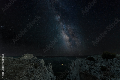 Night shot of the Milky Way with many stars in the Spanish province of Castille. In the foreground is a ravine on Mount Ardal. In the background the mountain landscape.