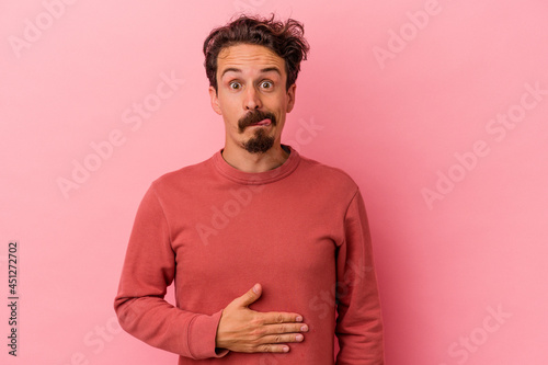 Young caucasian man isolated on pink background touches tummy, smiles gently, eating and satisfaction concept.