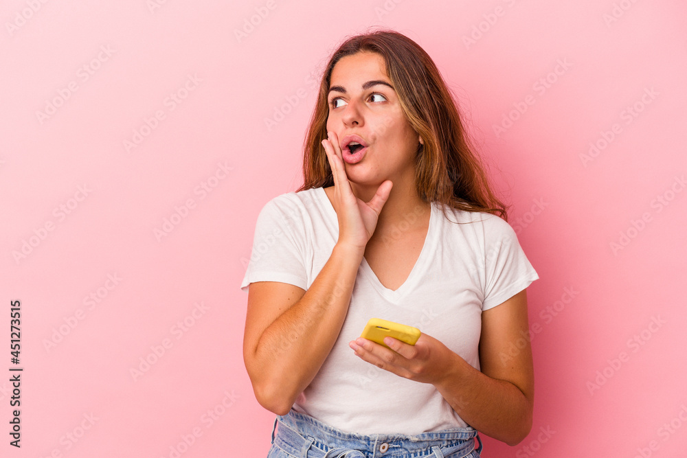 Young caucasian woman using mobile phone isolated on pink background is saying a secret hot braking news and looking aside Young caucasian woman using mobile phone isolated on pink background is saying a secret hot braking news and looking aside