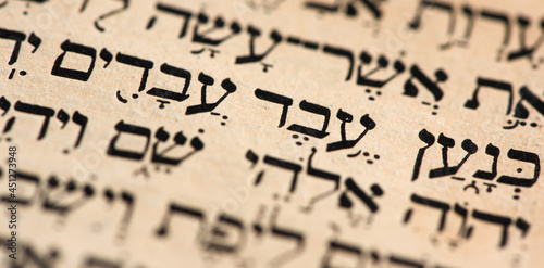 Closeup of hebrew words in Torah page that translate in english as Cursed be Canaan, a servant of servants shall he be to his brothers. Selective focus. Banner. photo
