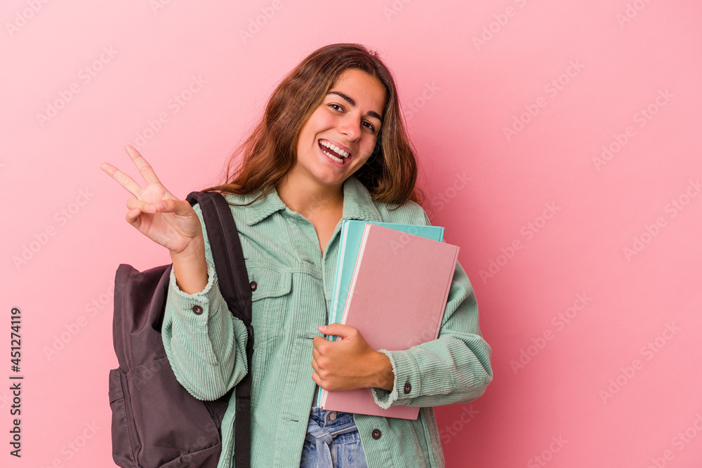 Young caucasian student woman holding books isolated on pink background joyful and carefree showing a peace symbol with fingers. Young caucasian student woman holding books isolated on pink background joyful and carefree showing a peace symbol with fingers.