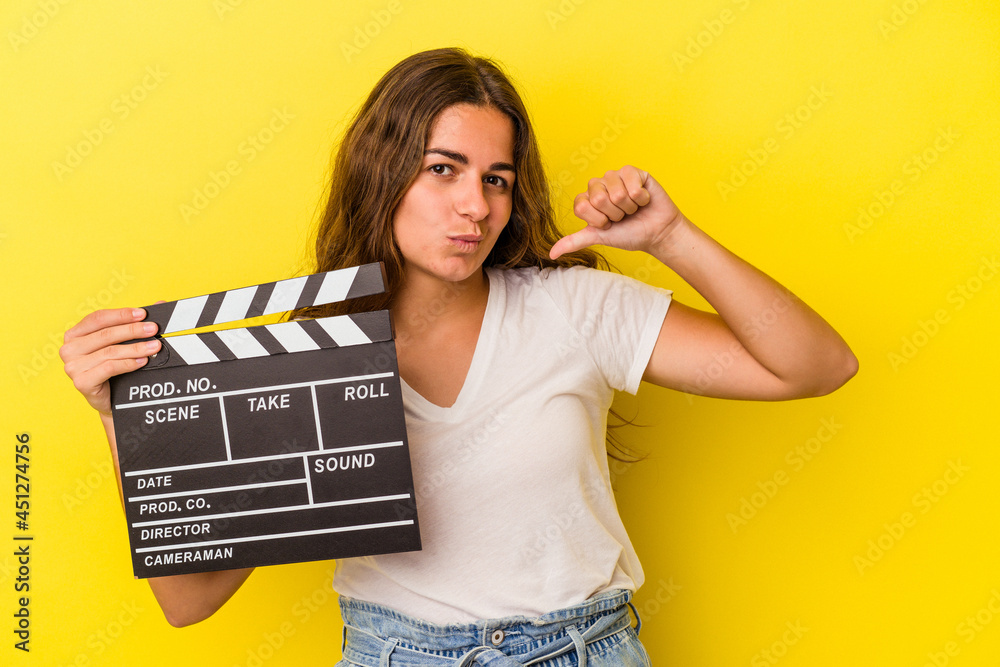 Young caucasian woman holding clapperboard isolated on yellow background  feels proud and self confident, example to follow.