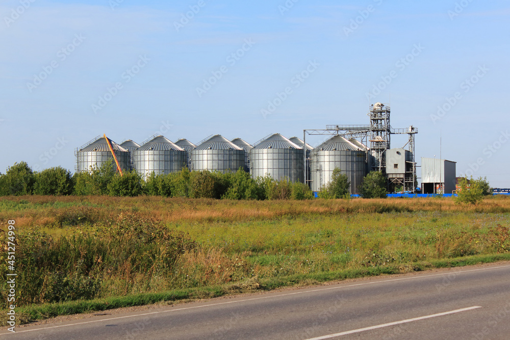 Grain elevator in rural zone. Modern agricultural grain elevator with blue sky on the background and roan on foreground. Grain elevator in rural zone. Modern agricultural grain elevator with blue sky on the background and roan on foreground.