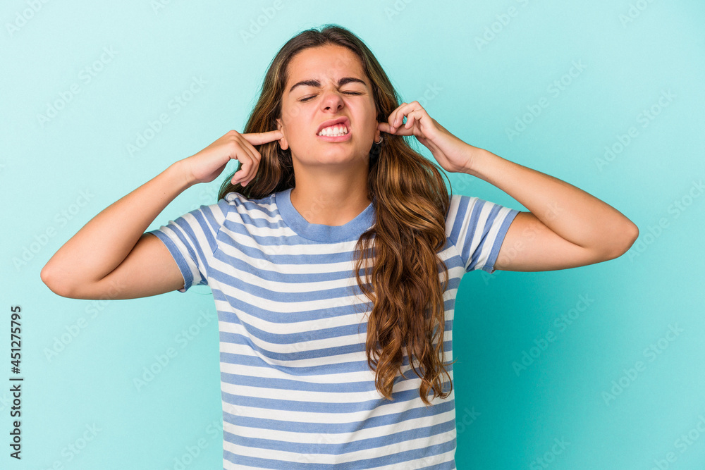 Young caucasian woman isolated on blue background covering ears with fingers, stressed and desperate by a loudly ambient. Young caucasian woman isolated on blue background covering ears with fingers, stressed and desperate by a loudly ambient.