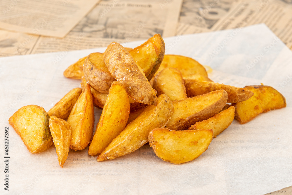 Portion of French fries cut into wedges with the skin and sea salt on white greaseproof paper