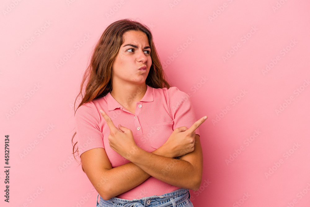 Young caucasian woman isolated on pink background points sideways, is trying to choose between two options. Young caucasian woman isolated on pink background points sideways, is trying to choose between two options.