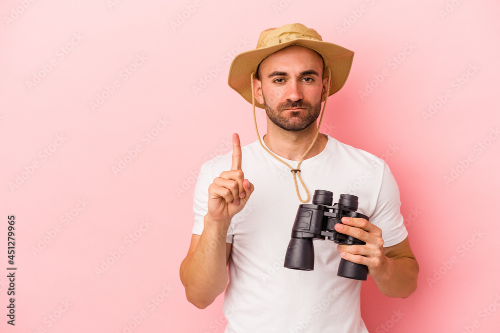 Young caucasian bald man holding binoculars isolated on pink background showing number one with finger. Young caucasian bald man holding binoculars isolated on pink background showing number one with finger.