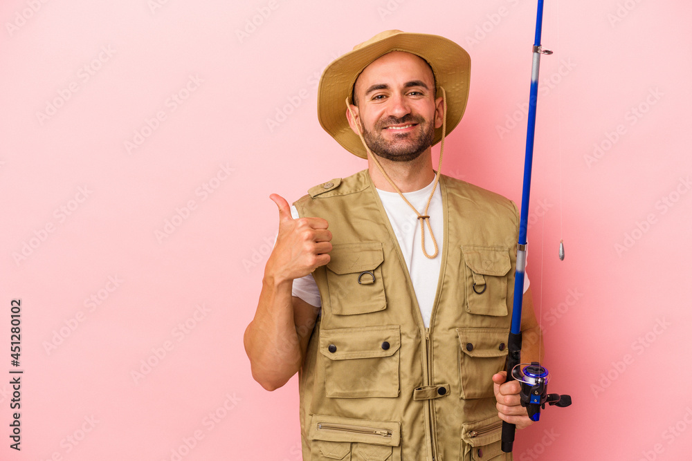 Young bald fisherman holding a rod isolated on pink background smiling and raising thumb up Young bald fisherman holding a rod isolated on pink background smiling and raising thumb up