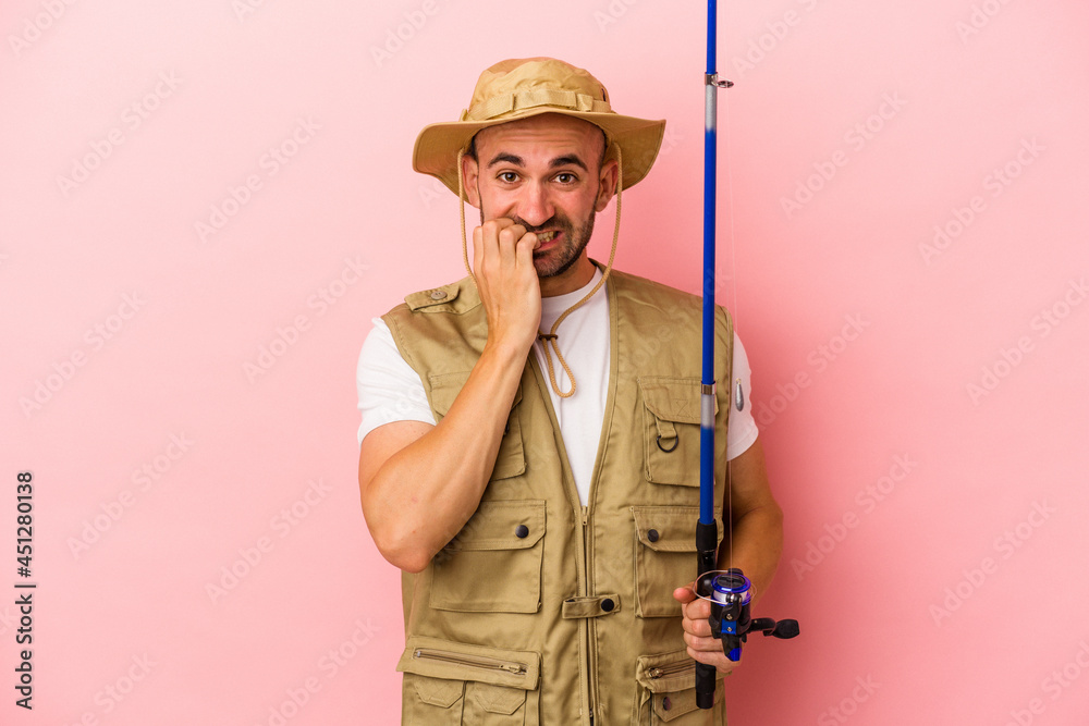 Young bald fisherman holding a rod isolated on pink background biting fingernails, nervous and very anxious. Young bald fisherman holding a rod isolated on pink background biting fingernails, nervous and very anxious.