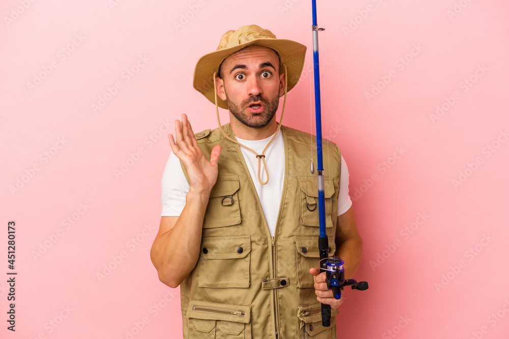 Young bald fisherman holding a rod isolated on pink background surprised and shocked. Young bald fisherman holding a rod isolated on pink background surprised and shocked.