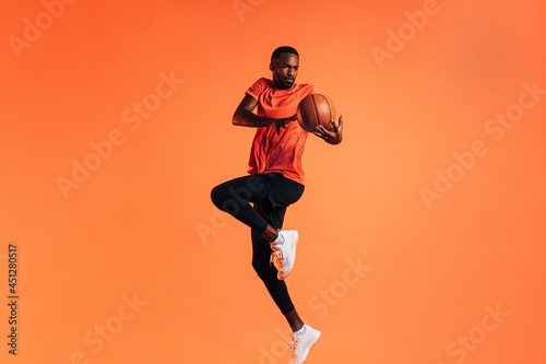 Sportsman jumping in studio against an orange background with basket ball