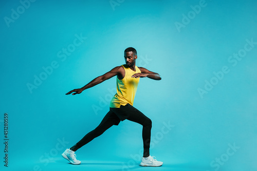 Young sportsman standing on blue background. Athlete warming up his body during a workout.