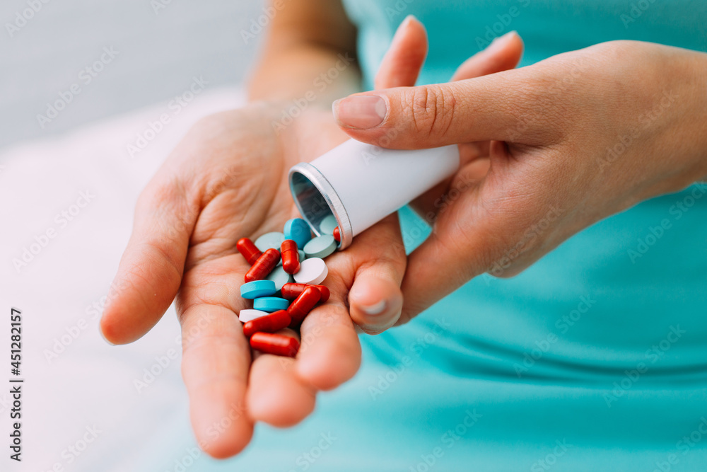 A woman takes out various pills and tablets from a container into her hand