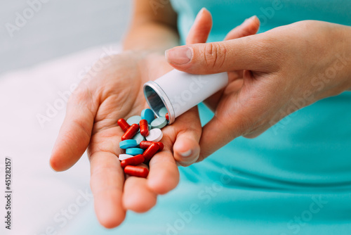 A woman takes out various pills and tablets from a container into her hand