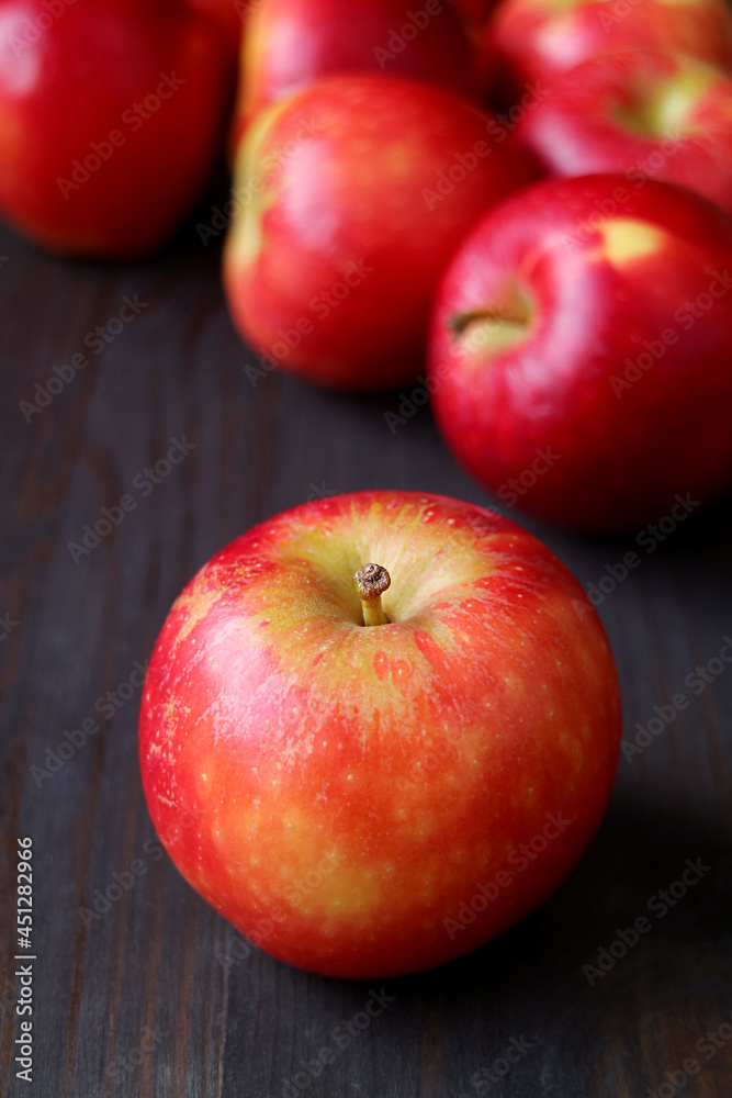 Closeup a fresh ripe apple with blurry heap of red apples on black wooden background Closeup a fresh ripe apple with blurry heap of red apples on black wooden background