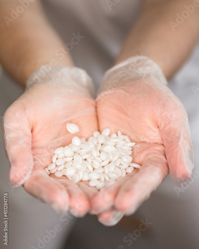 Close up view. A young woman holding in hands a white wax granules. White gloves