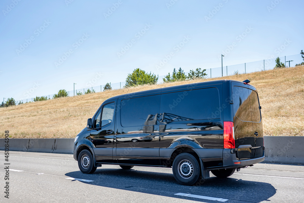Black compact commercial mini van for small business freights and local delivery running on the highway road to point of destination