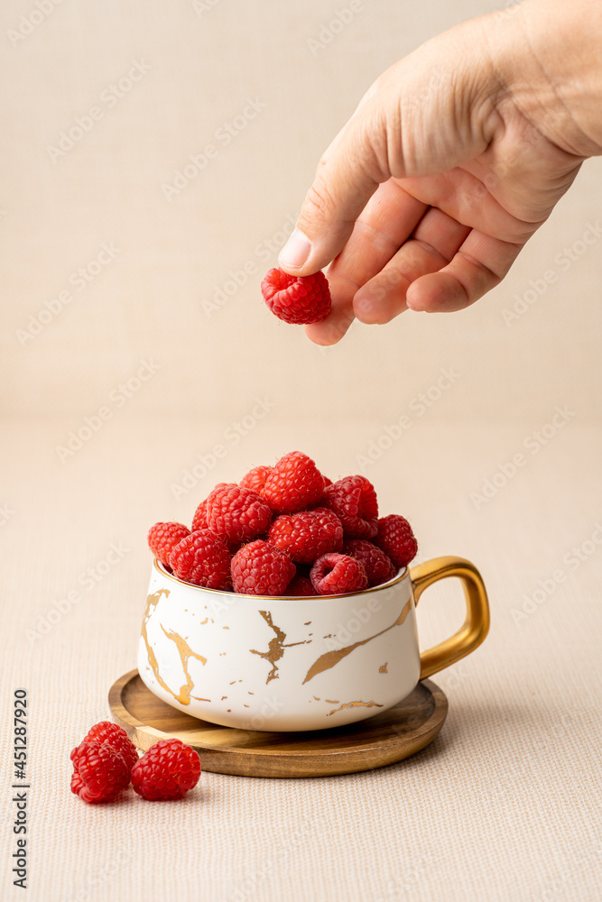 Raspberries in a cup with human hand in the frame dropping fruit Raspberries in a cup with human hand in the frame dropping fruit