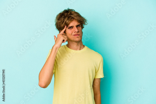 Young caucasian man with make up isolated on blue background pointing temple with finger, thinking, focused on a task.