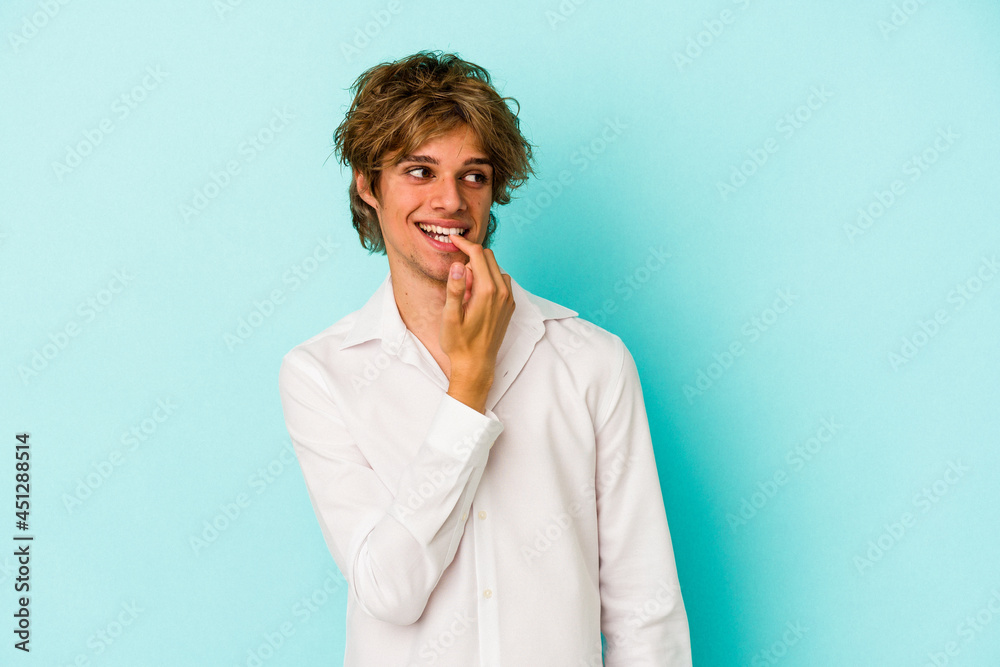 Young caucasian man with make up isolated on blue background  relaxed thinking about something looking at a copy space.
