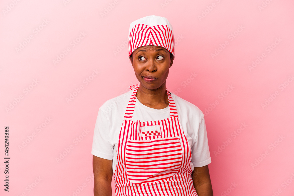 Young african american ice cream maker woman isolated on pink background confused, feels doubtful and unsure. Young african american ice cream maker woman isolated on pink background confused, feels doubtful and unsure.