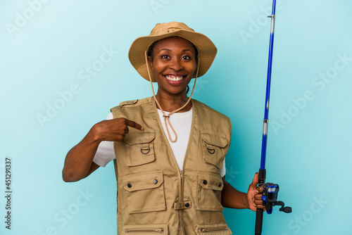 Young african american fisherwoman holding rod isolated on blue background person pointing by hand to a shirt copy space  proud and confident