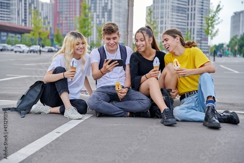 Group of teenagers with ice cream looking together at smartphone, urban style