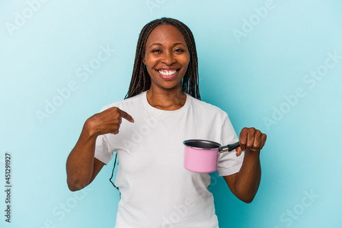 Young african american woman holding pan isolated on blue background person pointing by hand to a shirt copy space, proud and confident