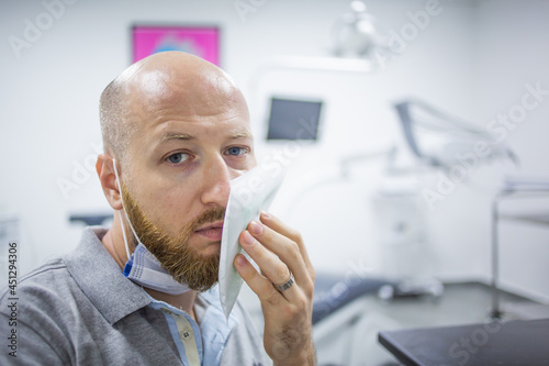 Unhappy and scared caucasian male in a dental clinic waiting for a check up and holding a cooling element at his cheek because of a toothache