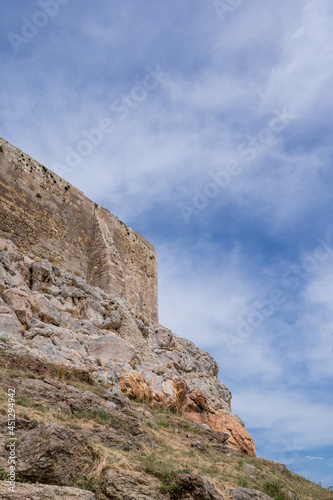 View from below of the Acropolis of Athens. High stone wall. Ancient Greek settlement. Landmark of Athens. Blue cloudy sky.