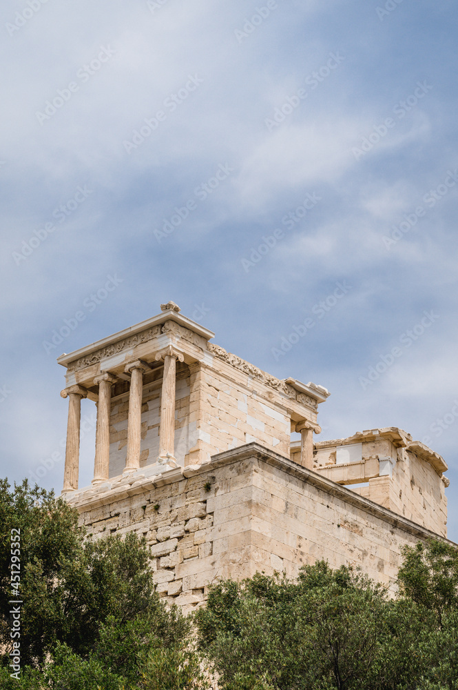 Bottom view of the ancient Greek temple on the Acropolis in Athens, Greece. Antique architecture. Blue cloudy sky. Green trees. Bottom view of the ancient Greek temple on the Acropolis in Athens, Greece. Antique architecture. Blue cloudy sky. Green trees.