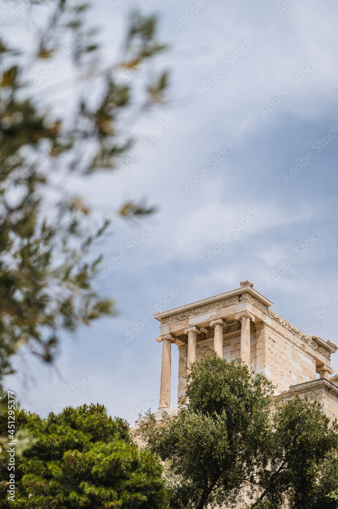 Bottom view of the ancient Greek temple on the Acropolis in Athens, Greece. Antique architecture. Blue cloudy sky. Green trees.