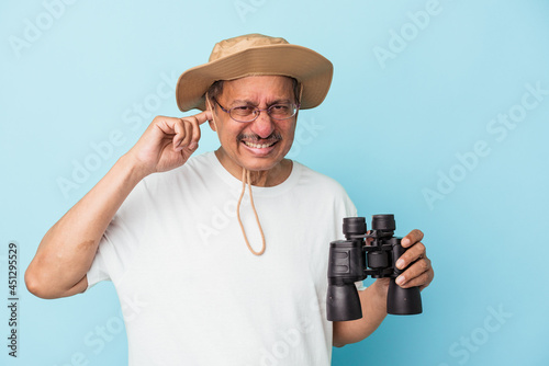 Middle aged indian fisherman holding rod isolated on blue background covering ears with hands.