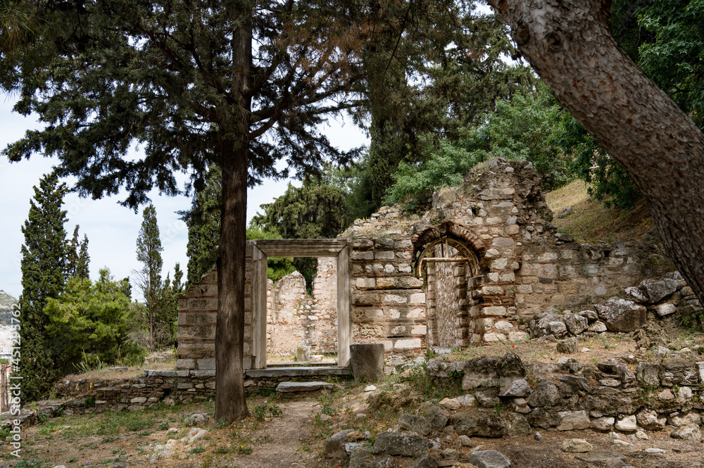 Ancient stone ruins between trees on slope of Acropolis hill.