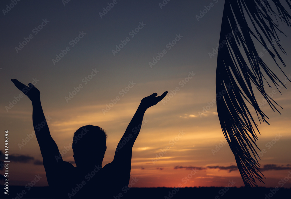 Beautiful sunset in the tropics with silhouettes of a man with his palms raised to the sky.