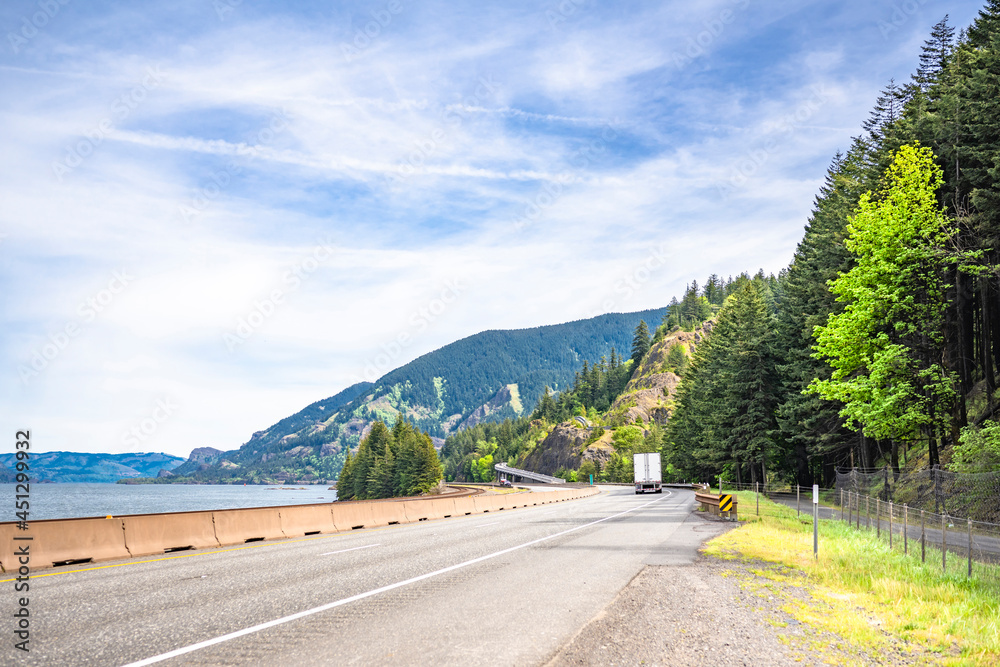 Winding highway road along the Columbia River with big rig semi truck and dry van semi trailer and another traffic in Columbia Gorge recreation area