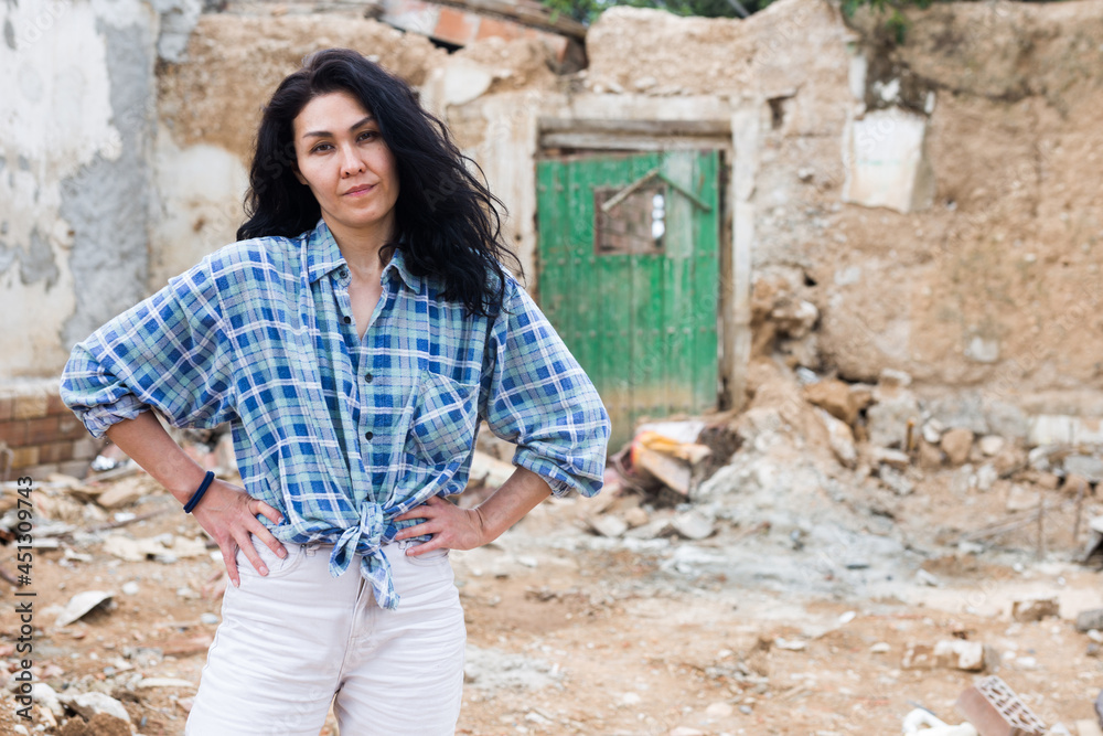 Portrait of adult asian woman standing in front of old ruined house after earthquake outdoors