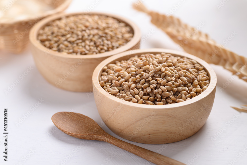 Wheat grain in a wooden bowl and spoon on white background