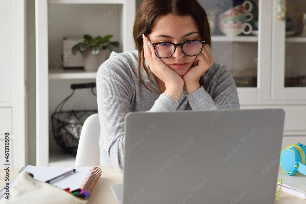Young girl student looking bored while studying at home using laptop computer Young girl student looking bored while studying at home using laptop computer