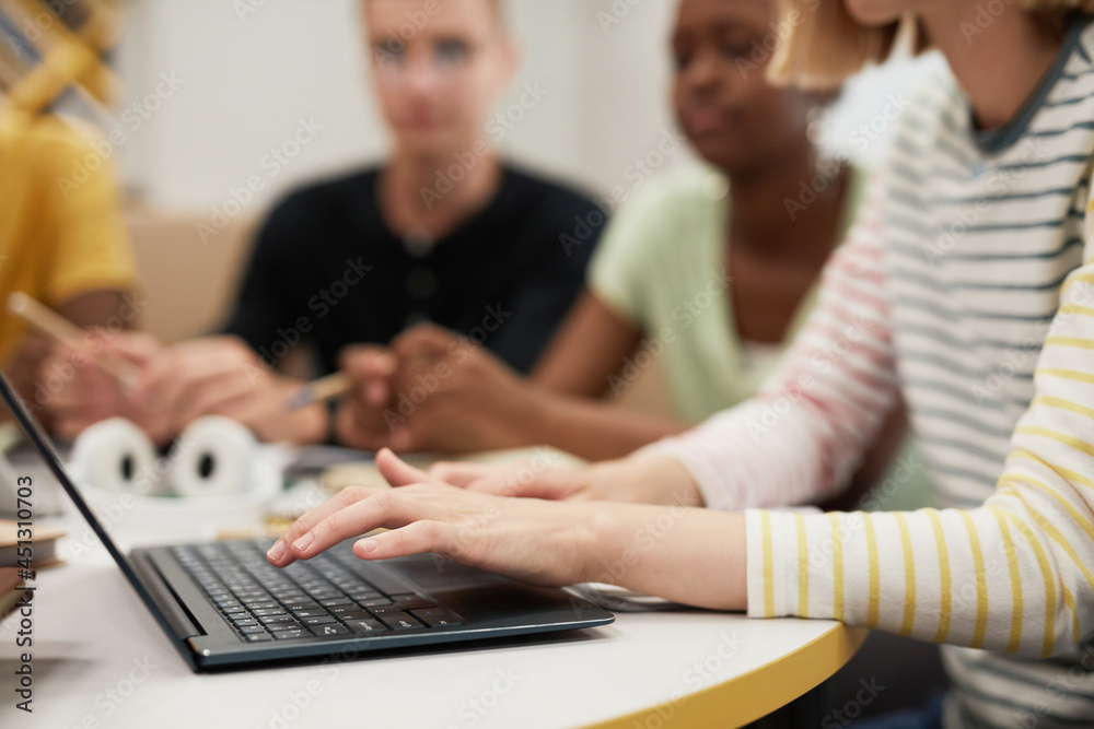 Side view close up at diverse group of young people studying together at table in college library, focus on female hands typing at laptop keyboard, copy space Side view close up at diverse group of young people studying together at table in college library, focus on female hands typing at laptop keyboard, copy space